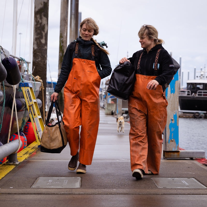 Emma and Claire, the Salmon Sisters, walking down a wharf in Alaska wearing their fishing gear
