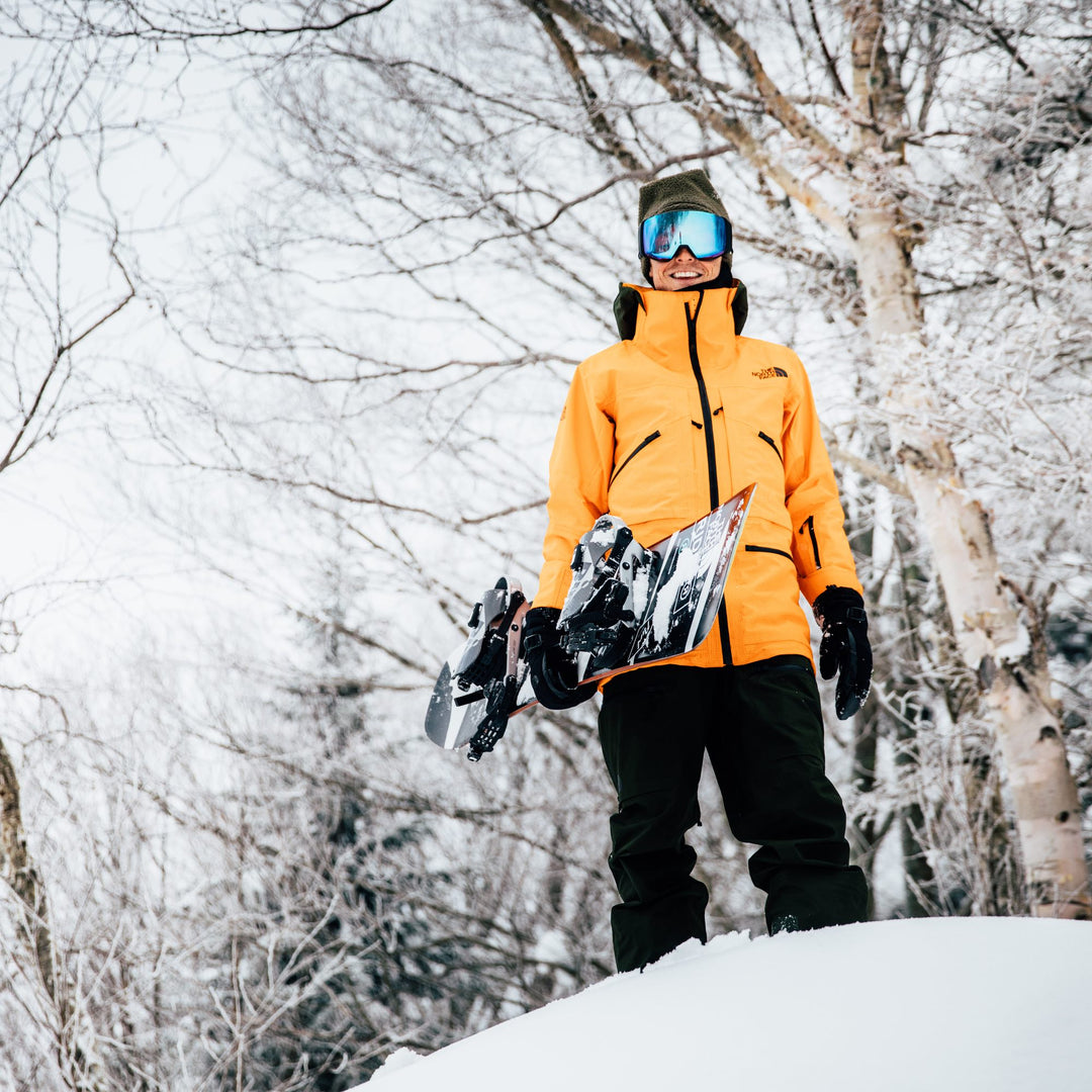 Jake Blauvelt, professional snowboarder, standing in the snow holding his snowboard