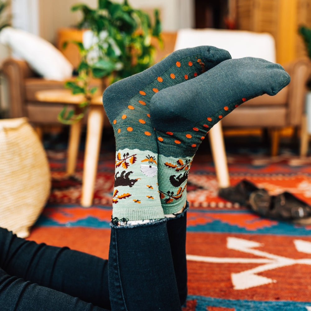 Crossed feet in the air wearing merino wool socks with a bear and fall leaves