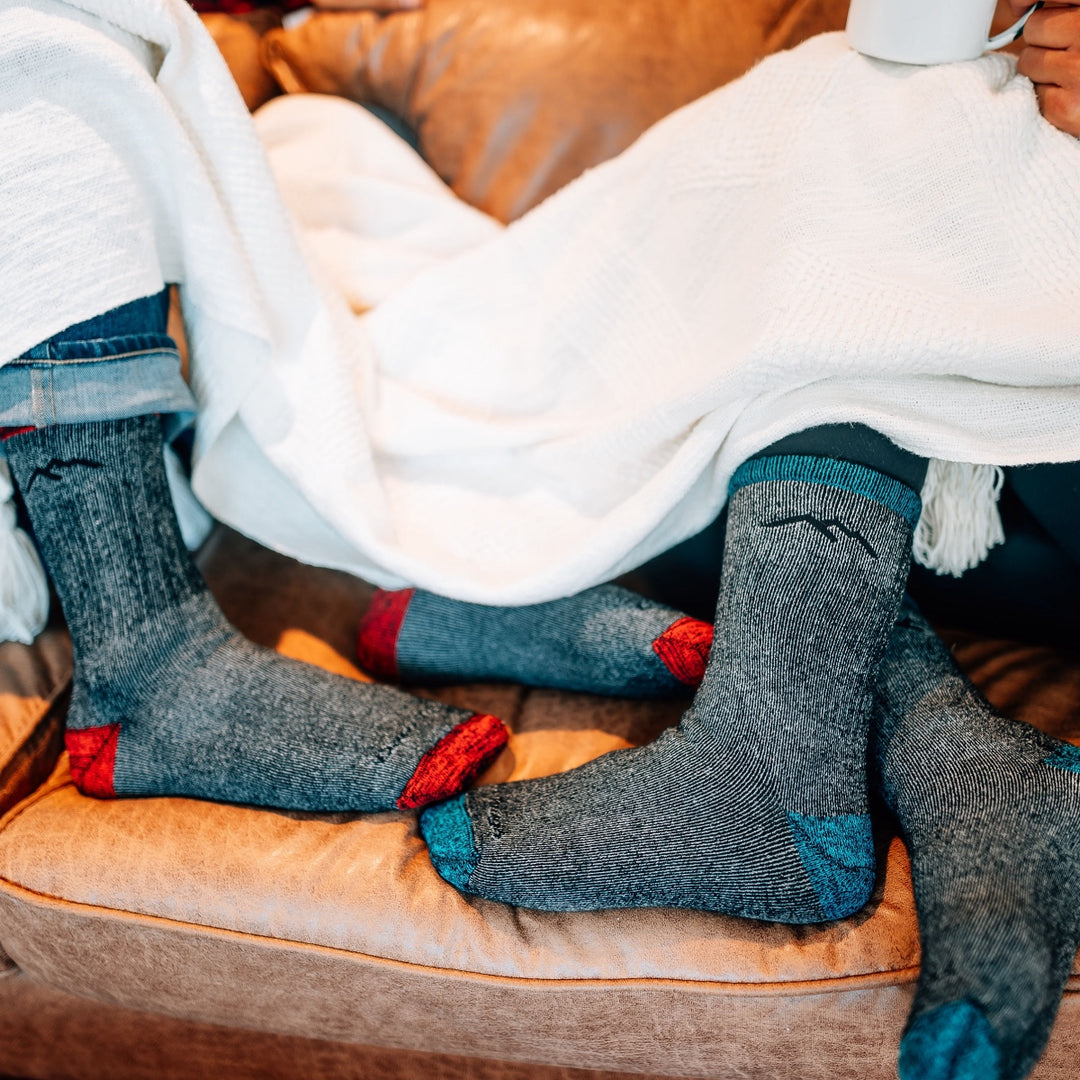 Two pairs of feet sticking out from under a blanket, wearing super soft merino wool socks, no itch