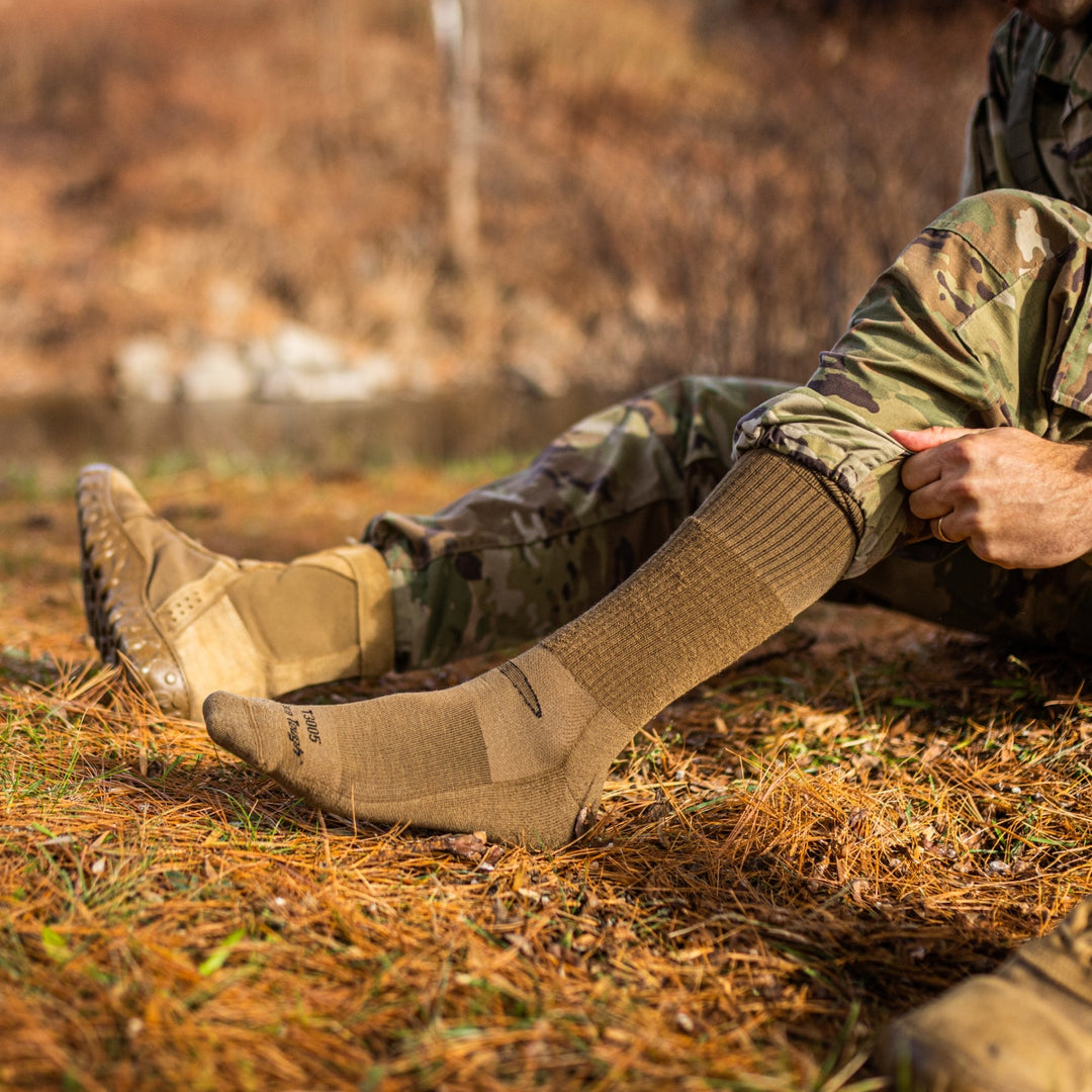 Person in combat fatigues pulling on tan darn tough tactical socks
