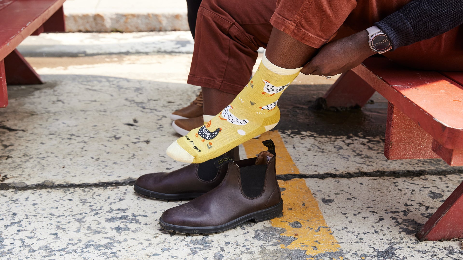 A picture of a woman putting on a pair of women's mother clucker lifestyle socks with hens, egg, and chicken designs.