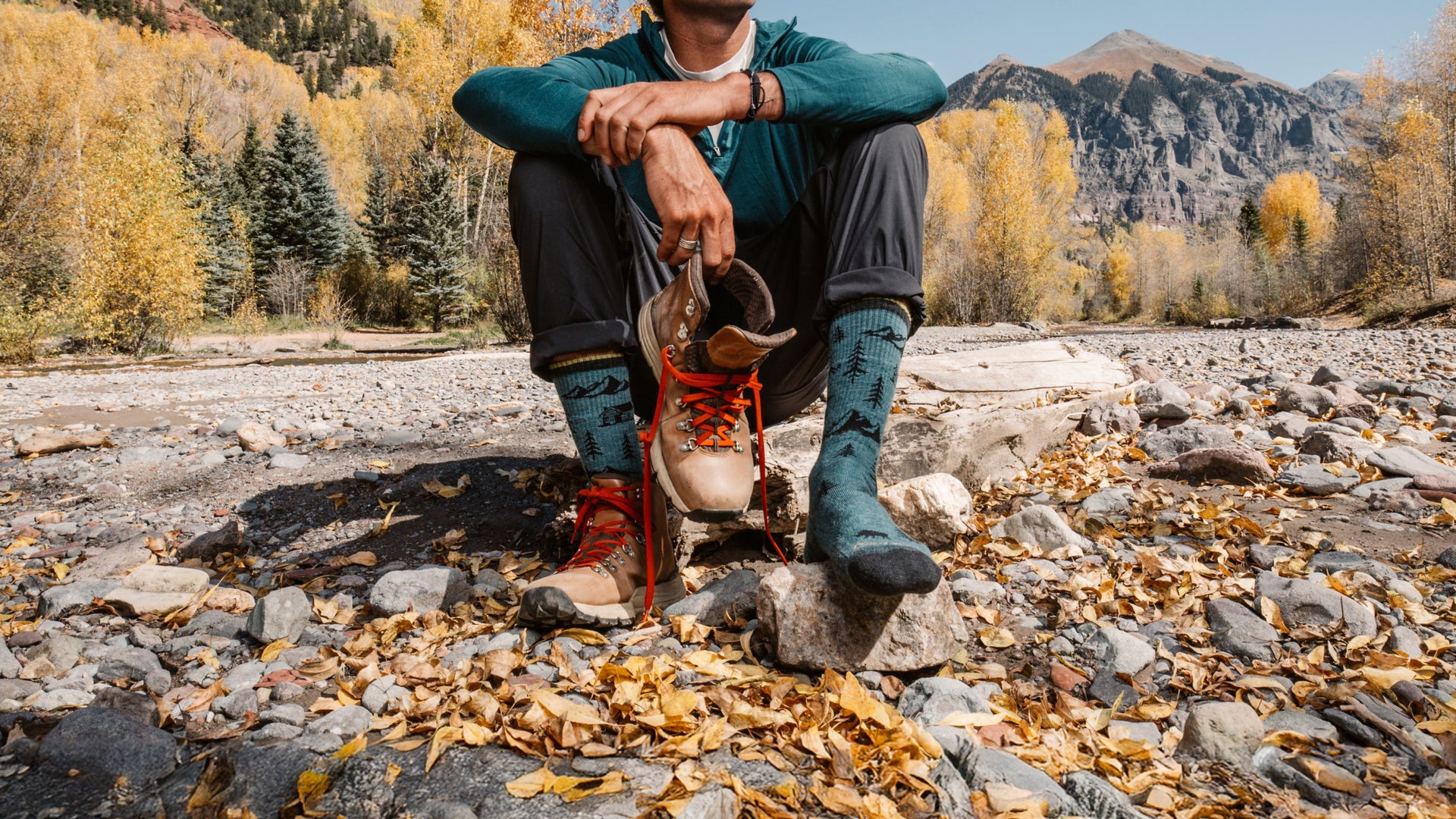 Model sitting on the rocks next to a river wearing the ABC boot sock