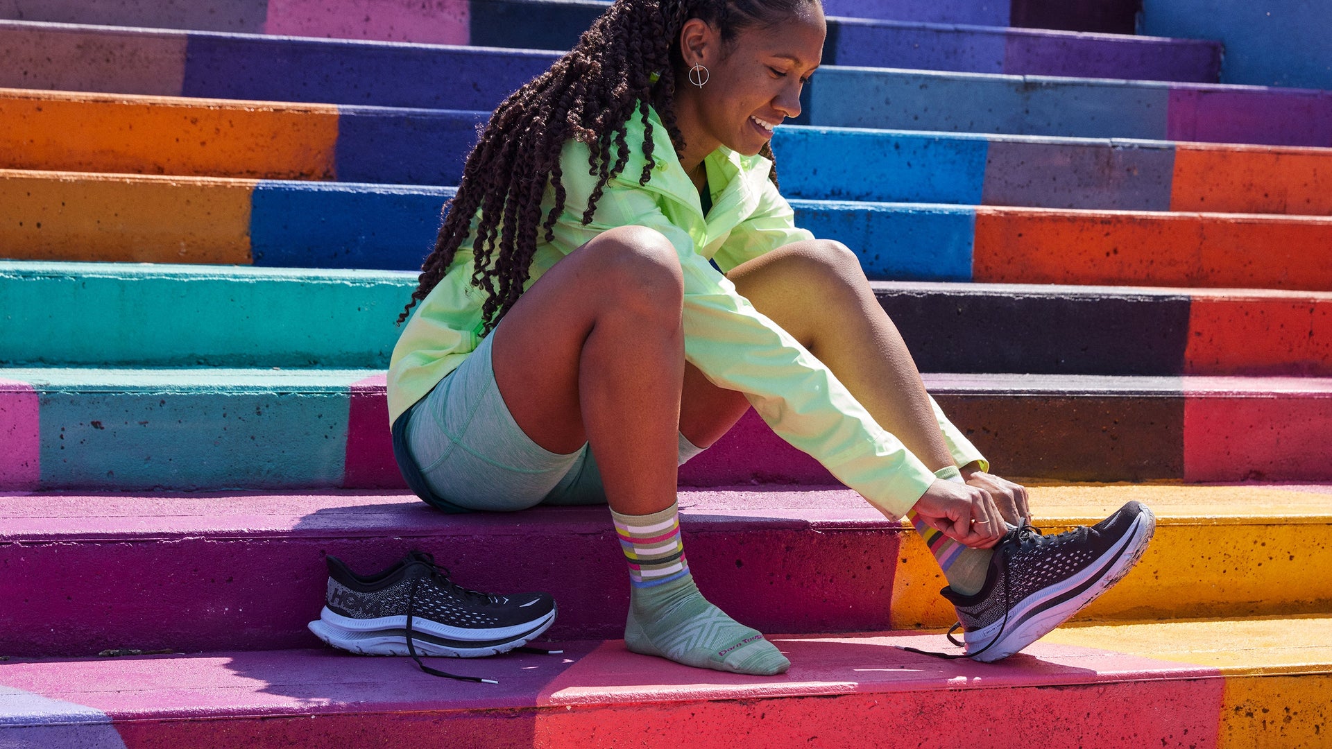 Women setting on stairs putting sneakers on wearing the relay micro crew