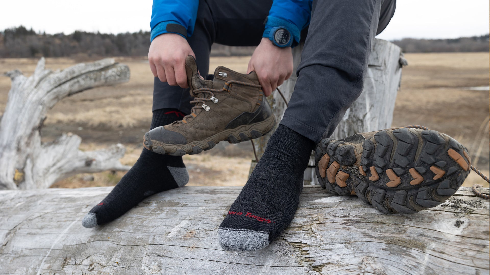 Man whittling by fire wearing boots and darn tough men's socks, warm merino wool socks for men