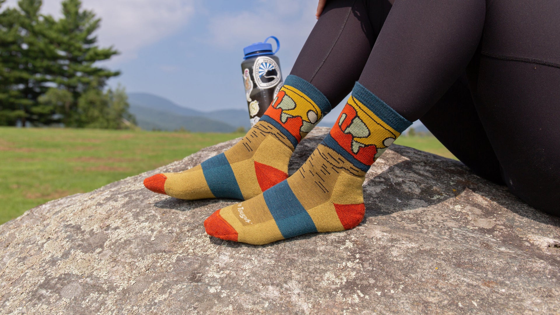 Model sitting on a rock with feet up wearing the celeste micro crew hiking sock