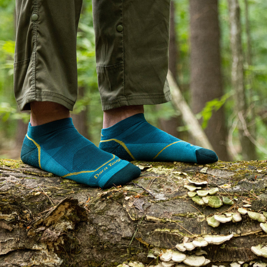 Close up shot of model standing on a log wearing the men's light hiker no show hiking sock in cascade blue