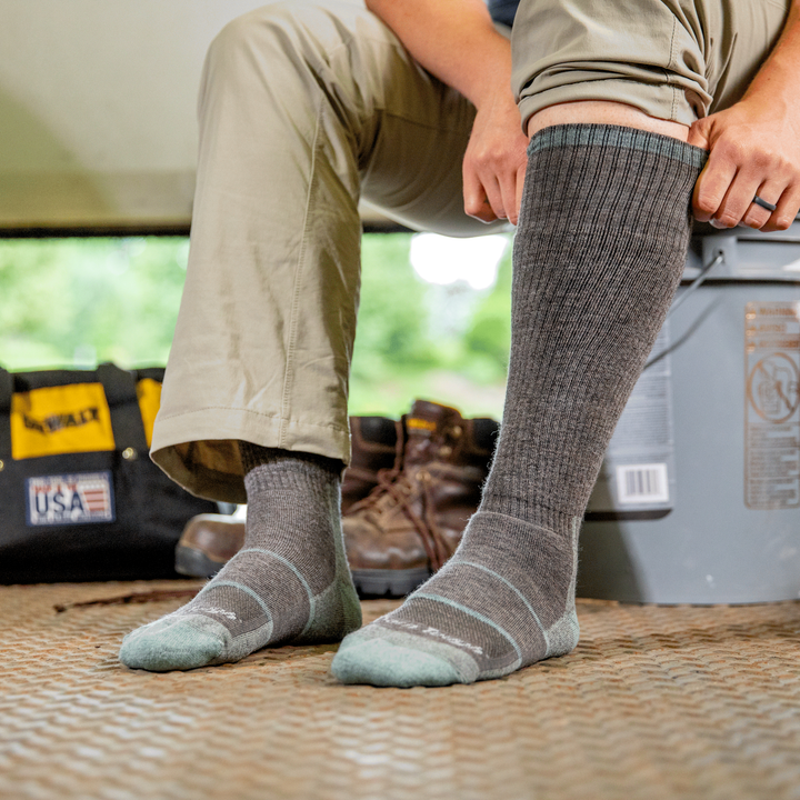 Woman pulling on Mary Fields over the calf work socks in shale gray