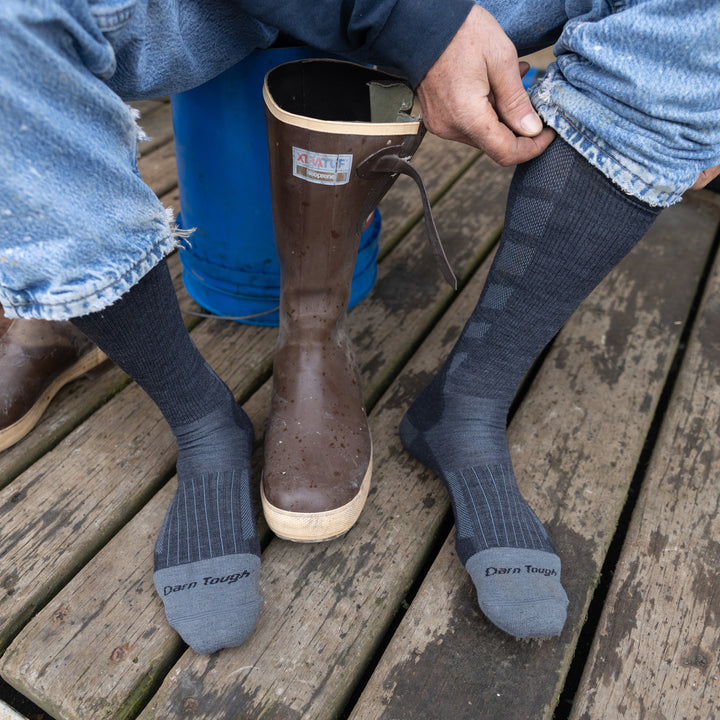 Overhead shot of model putting on the men's stanley k mid-calf work sock in gravel with brown rain boots