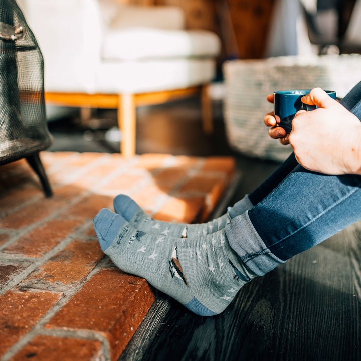 Model sitting with her feet up against brick wearing women's twitterpated crew lifestyle sock in seafoam