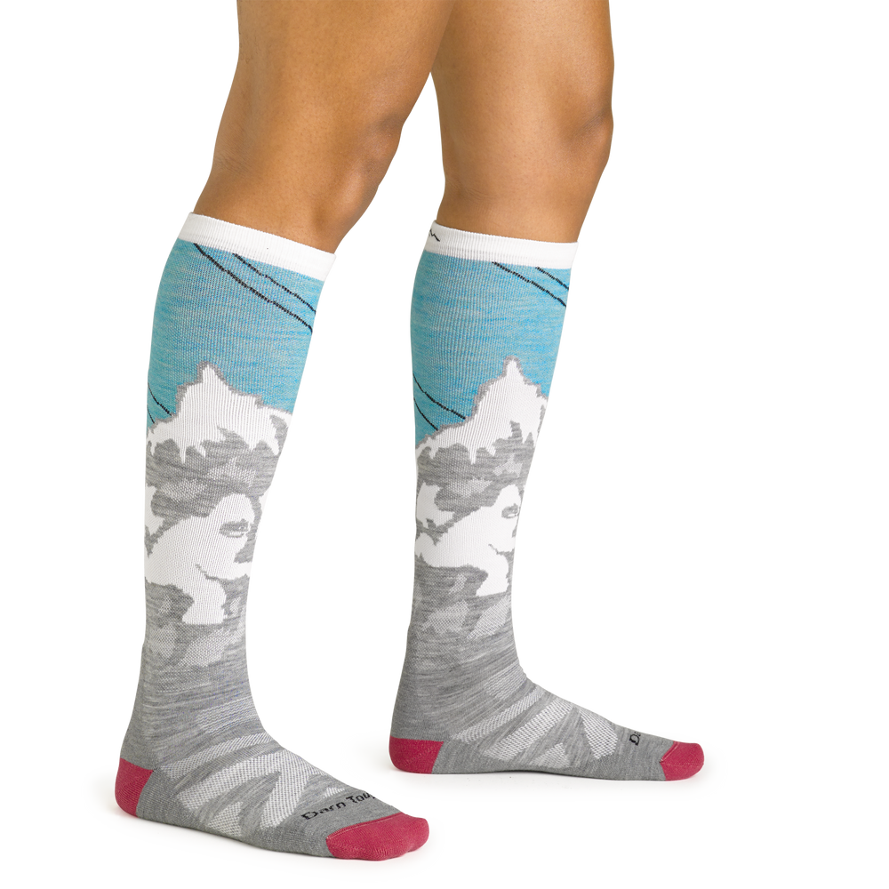 Close up studio shot of model wearing women's yeti over-the-calf midweight ski & snowboard sock in aqua