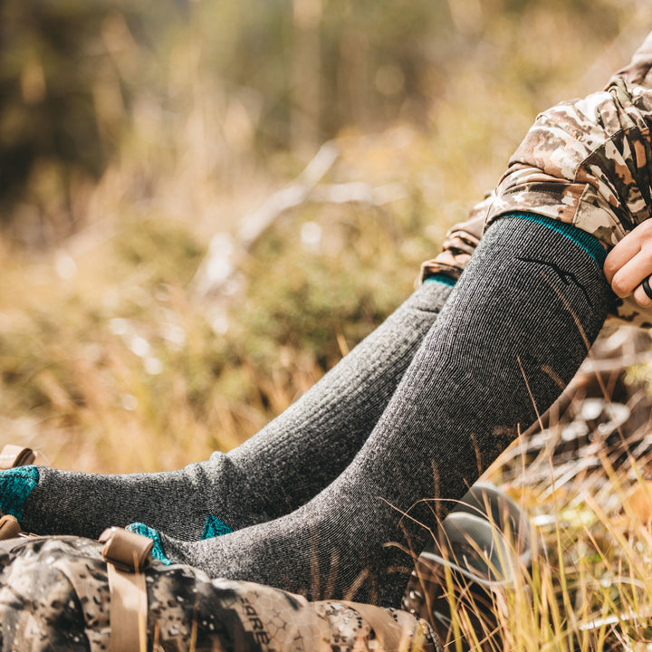 Woman wearing camo hunting gear and Women's Mountaineering Over the Calf Heavyweight Hiking Socks in Midnight