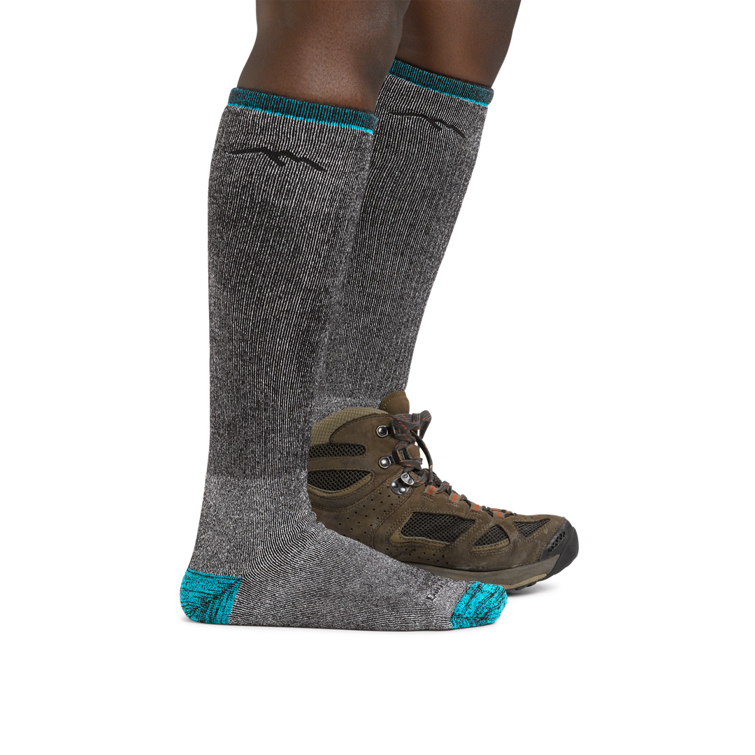 Woman wearing Women's Mountaineering Over the Calf Heavyweight Hiking Socks in Midnight with one foot  in a hiking boot