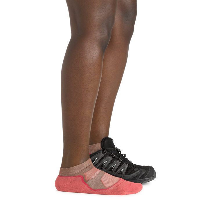 Profile image of a woman's legs on a white background, wearing Women's Light Hiker No Show Lightweight Hiking Socks in Canyon colorway, with one foot also in a hiking shoe