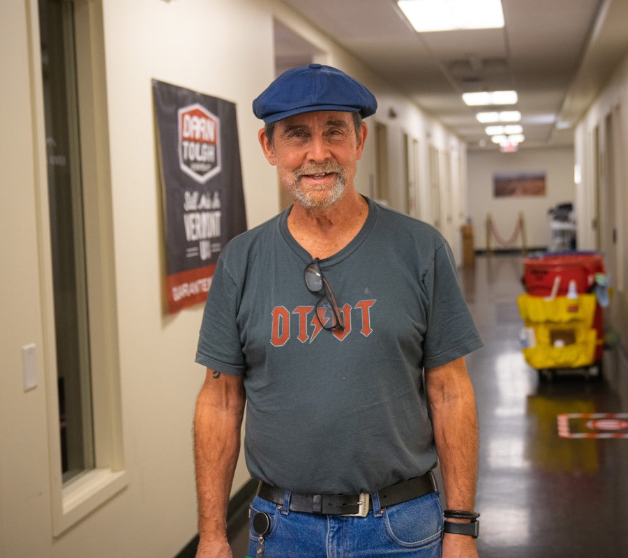 Peter smiling at the camera wearing his newsboy cap and Darn Tough shirt