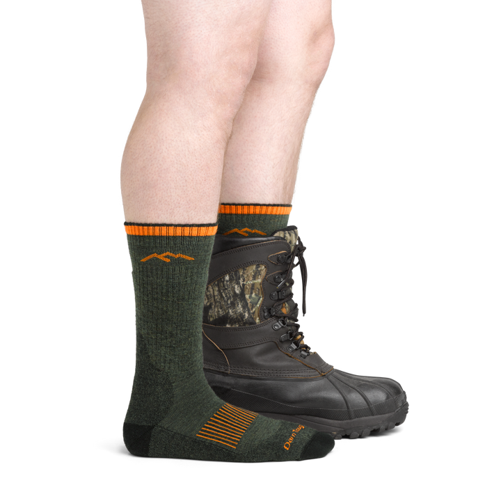 Image of model wearing 2111 Midweight Hunting Boot Socks in Forest colorway with camo hunting boot on one foot
