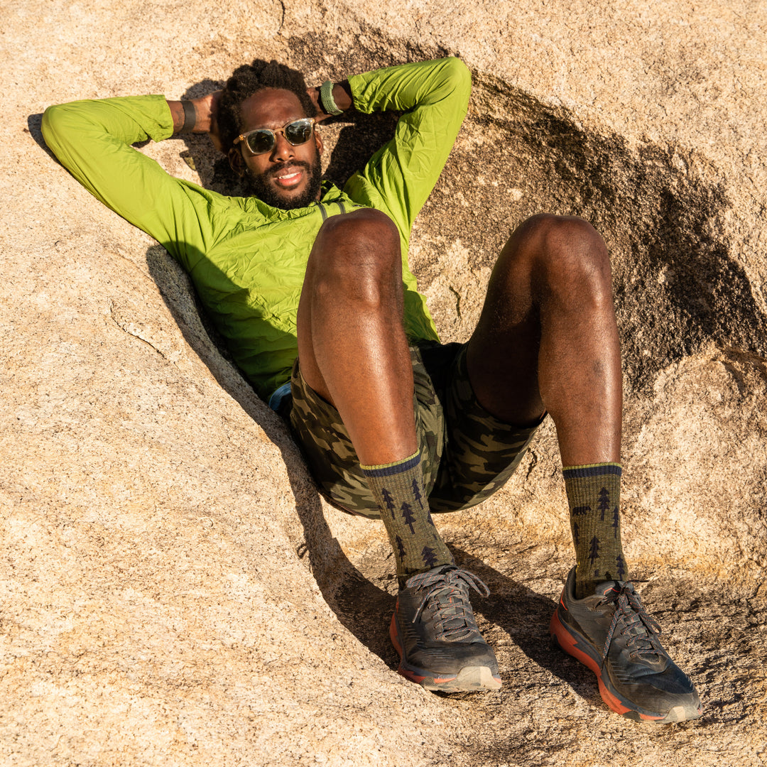 Full body shot of model laying down on rocks in Joshua Tree National Park while wearing the men's ABC boot sock in forest