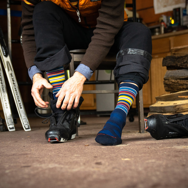 Close up shot of model sitting ouside putting on black snow shoes wearng the men's oslo nordic boot snow sock in eclipse blue