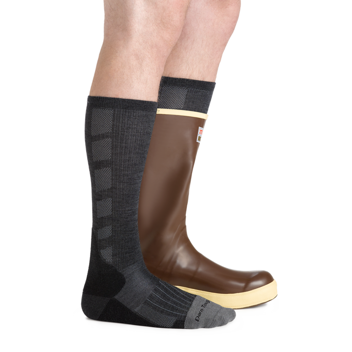 Side studio shot of model wearing men's stanley k mid-calf work sock in gravel gray with Rubber boot on left foot