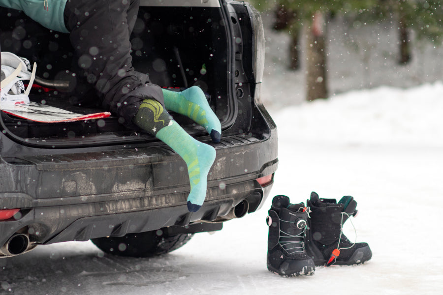 A skier wearing darn tough socks, climbing into back of their car for more gear