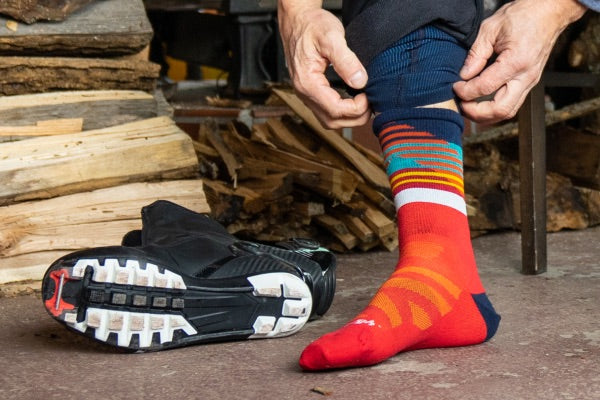 Nordic skier pulling on cross country ski socks, with ski boots next to them