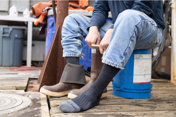 Person on boat deck wearing darn tough socks for work and pulling on rubber boots