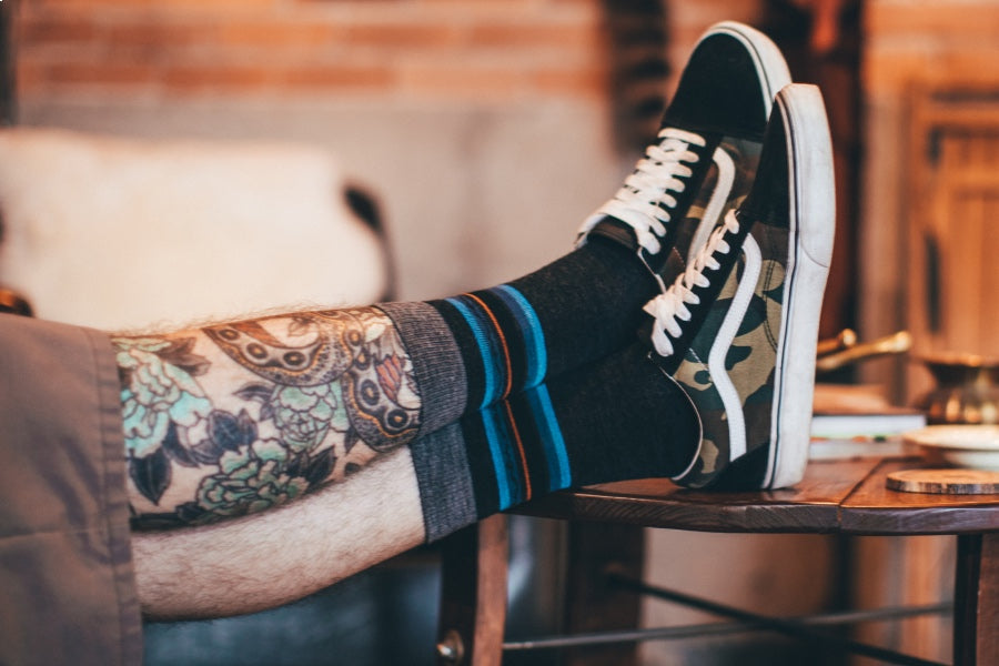 A pair of feet relaxing on the table top wearing striped everyday socks and casual sneakers