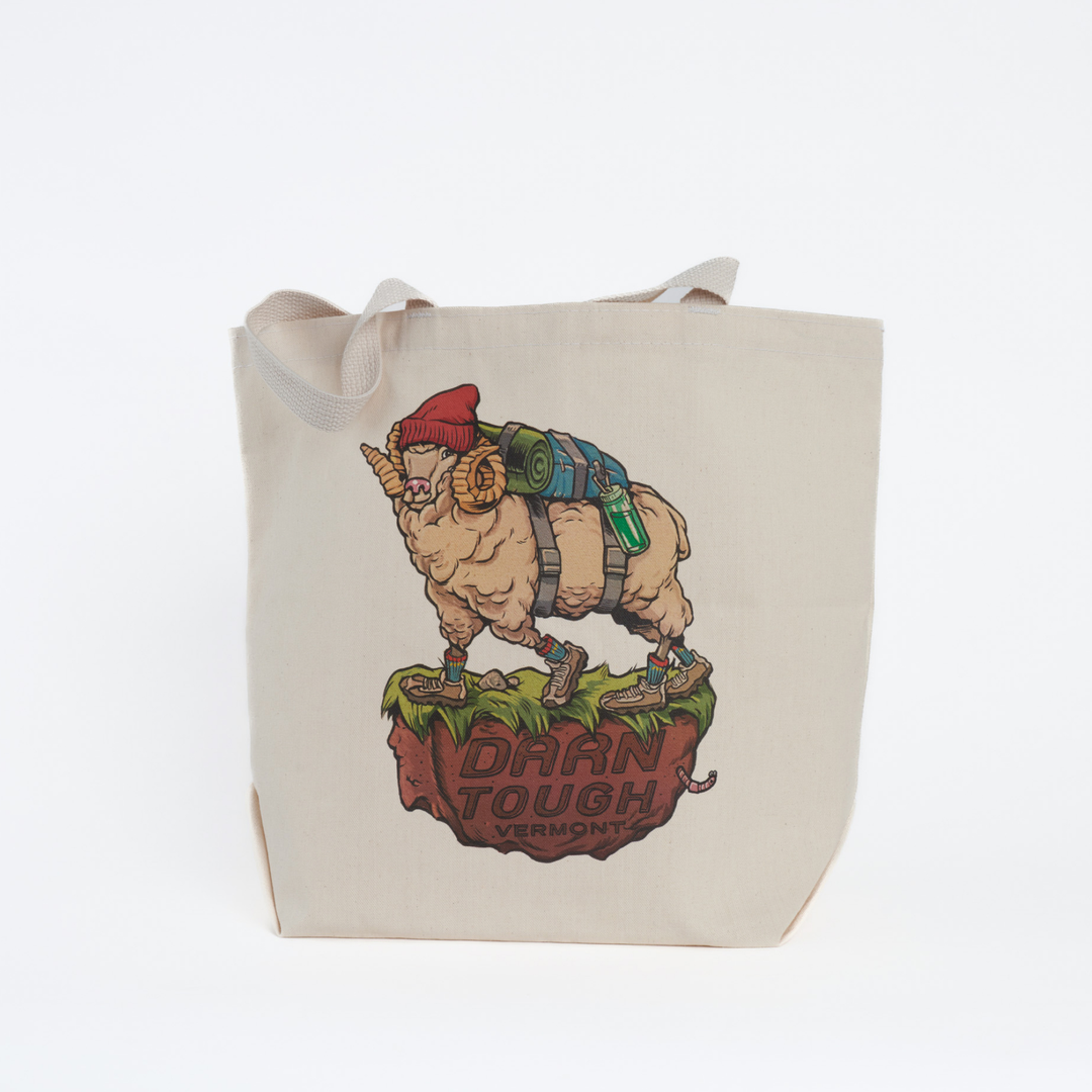 canvas tote bag with straps tucked in, front of bag features art work of a northern ram wearing a hat and back pack