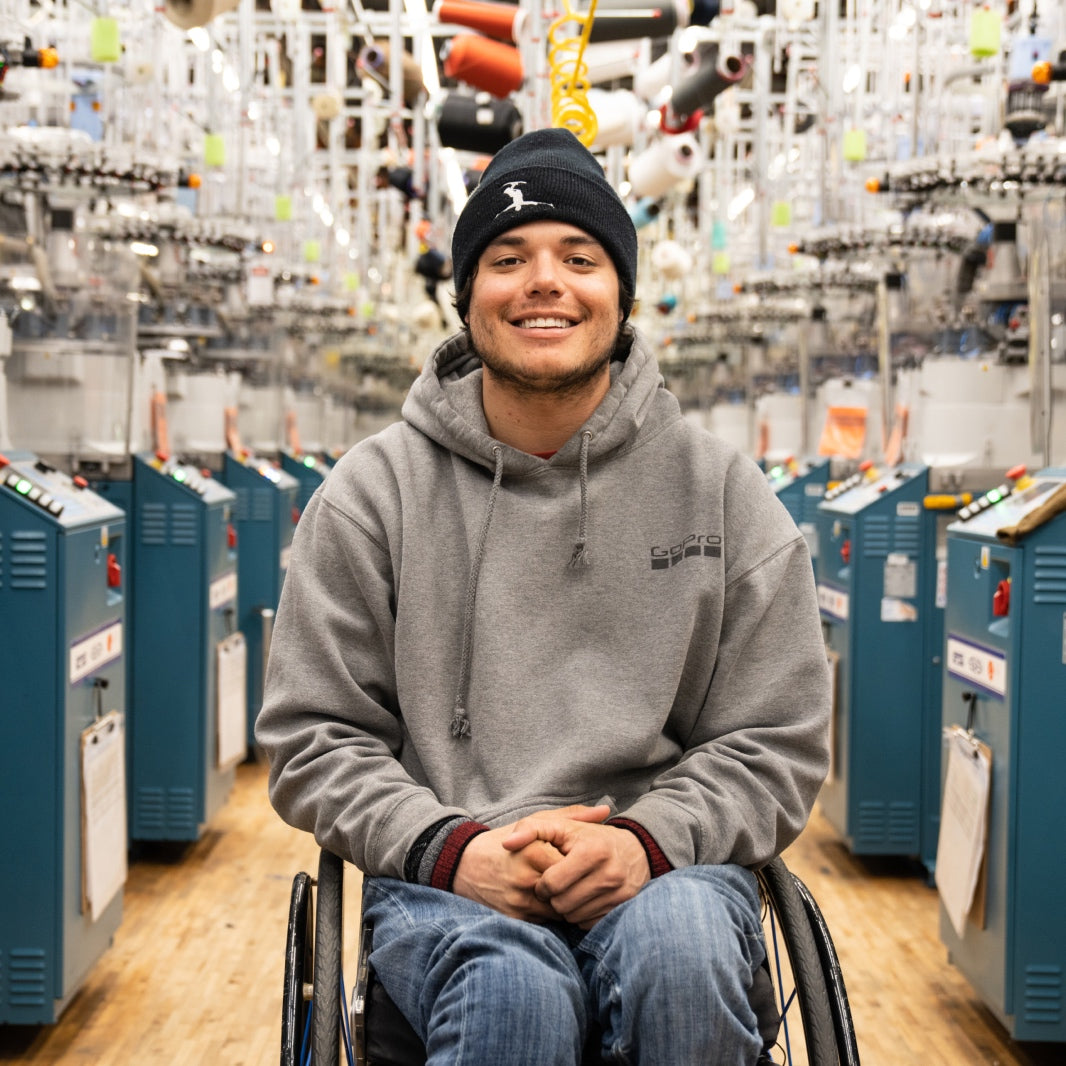Trevor at the Darn Tough Mill, seated in his wheelchair surrounded by knitting machines