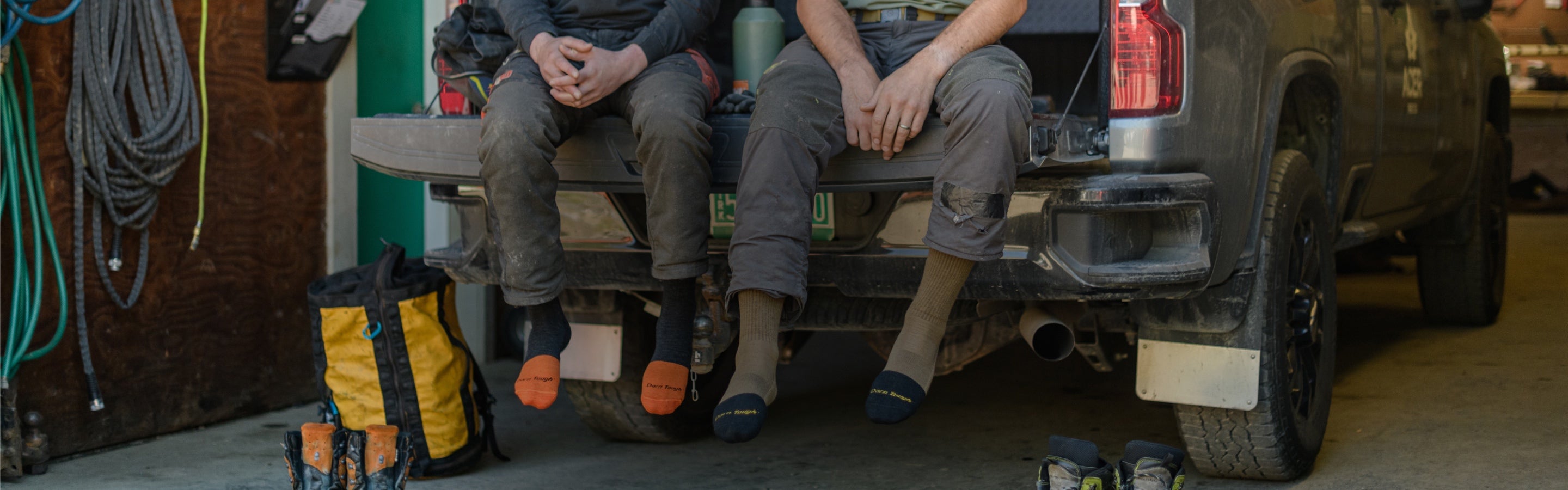 Two people seated on truck bed at a job site wearing work socks