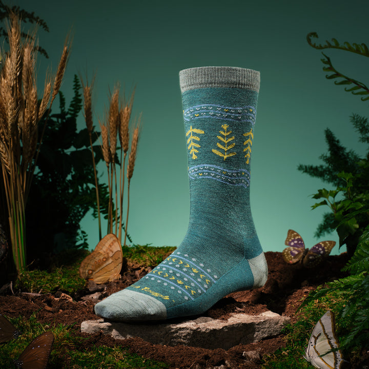 nature image with the grain or shine crew sock on foot form in the middle with moss ground and wheat stocks around it