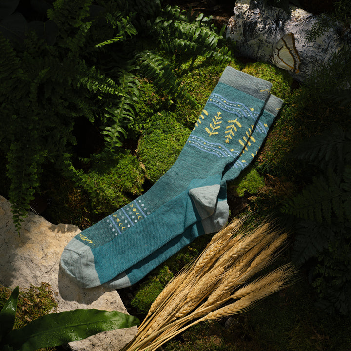 lay flat image of the grain or shine crew sock laying on moss with wheat stocks next to it