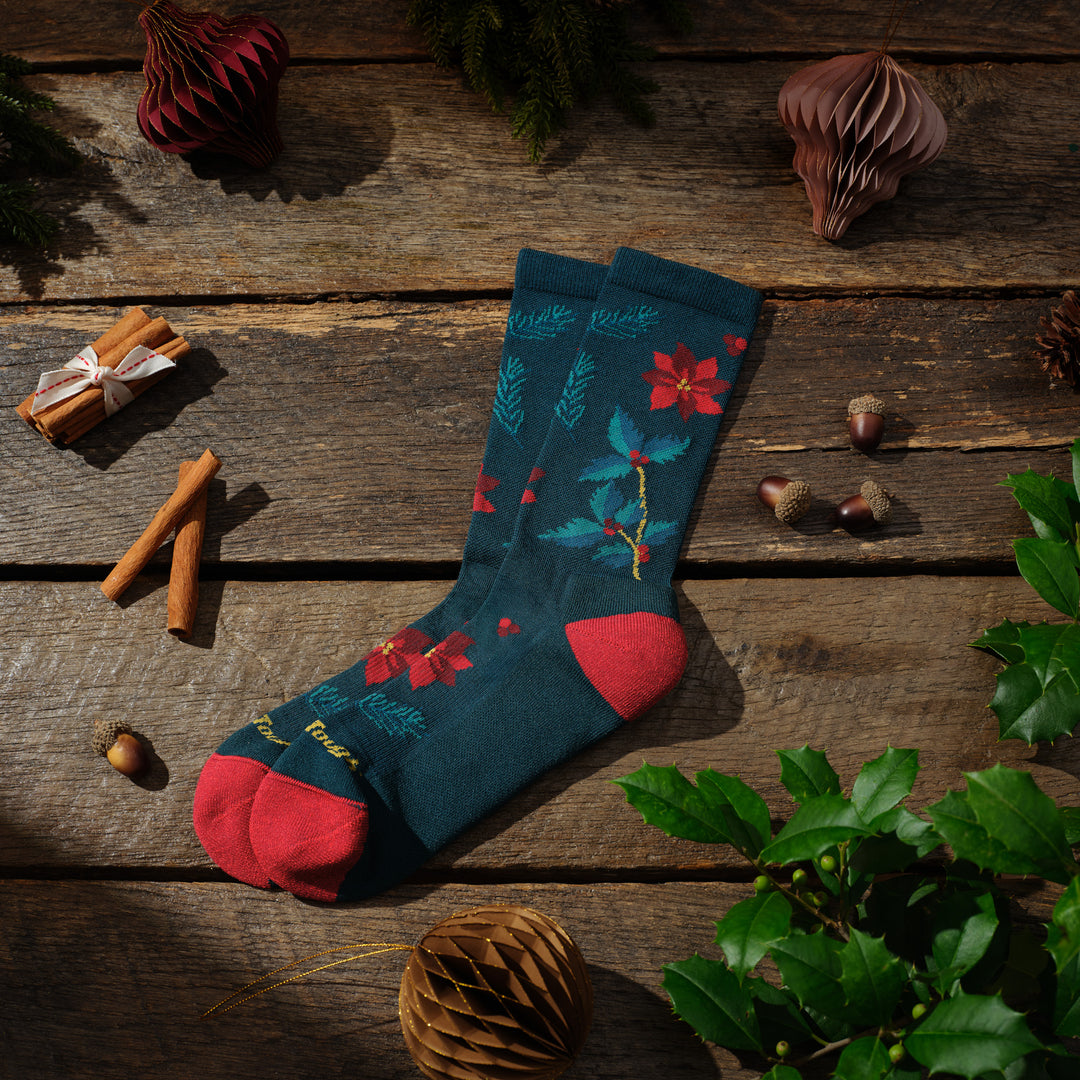 pair of mistle toe crew sock laying on wood floor with nuts and cinnamon sticks