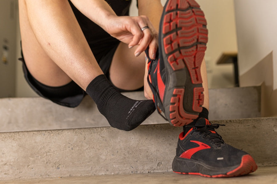 Person putting on running sneakers over ankle height tactical socks in black