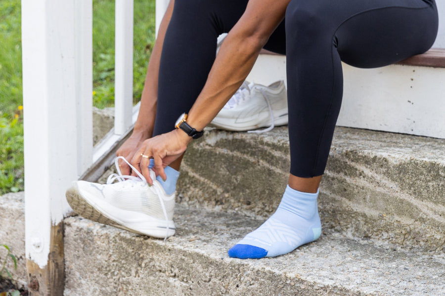 Person seated on step wearing running socks, pulling on running sneakers
