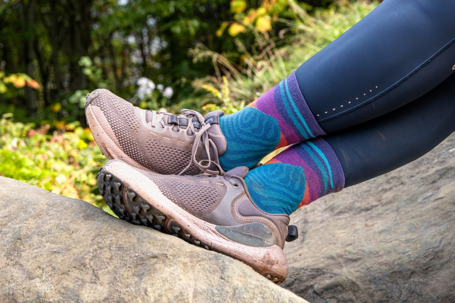 Feet wearing the Mirnavated sock, featuring a blue mountain design with a sunset in hues of purple and pink