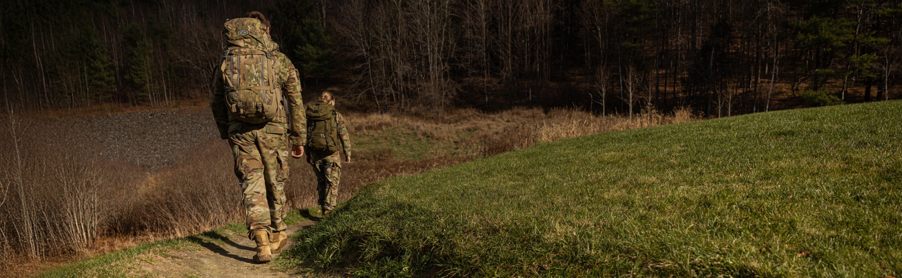 Two people in military uniform hiking across grassy terrain