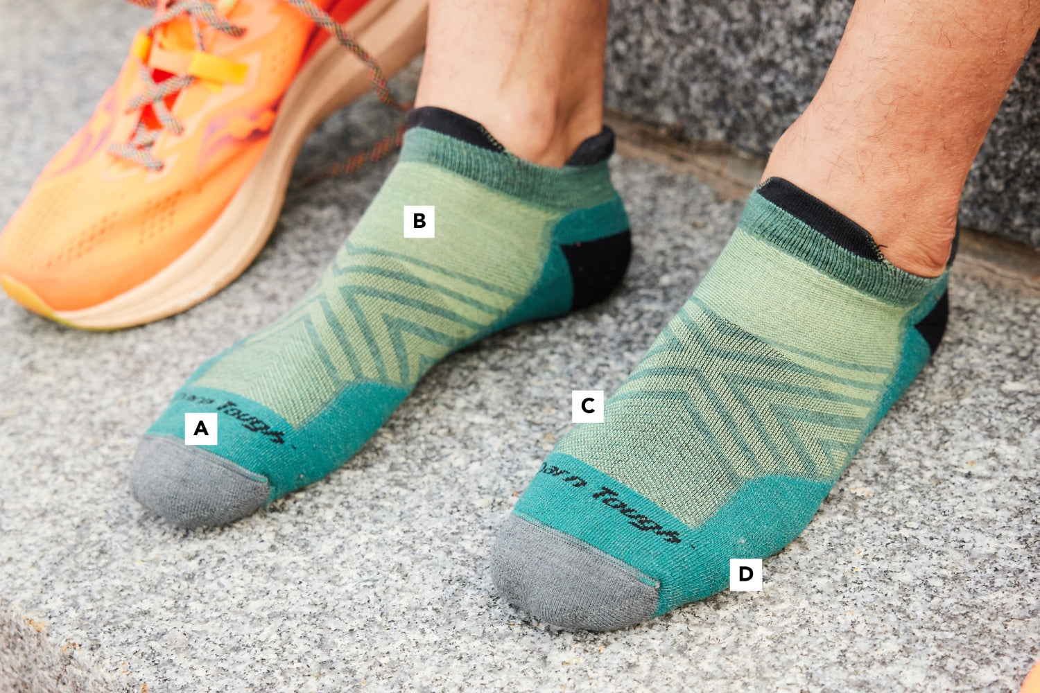 A pair of feet wearing Darn Tough run socks with small callouts showing different features