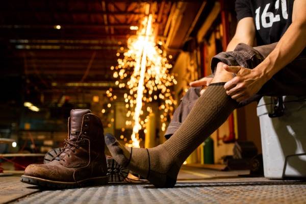 Man in factory pulling on darn tough thick socks for work and work boots