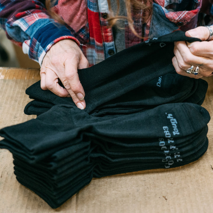 A stack of black quarter socks being folded by a Darn Tough employee