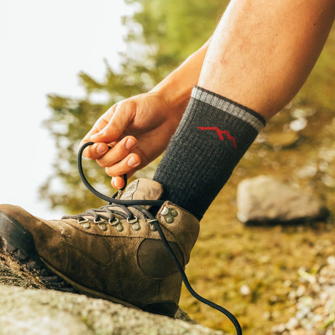 Side shot of a model sitting down tying their brown hiking shoe wearing the men's boot hiking sock in black