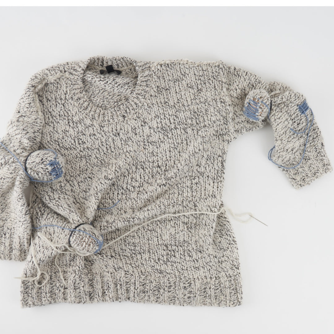 A knit sweater with several holes getting darned