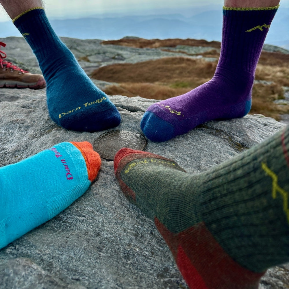 Four feet each wearing a different color of the Hiker Micro Crew socks standing on a mountain top