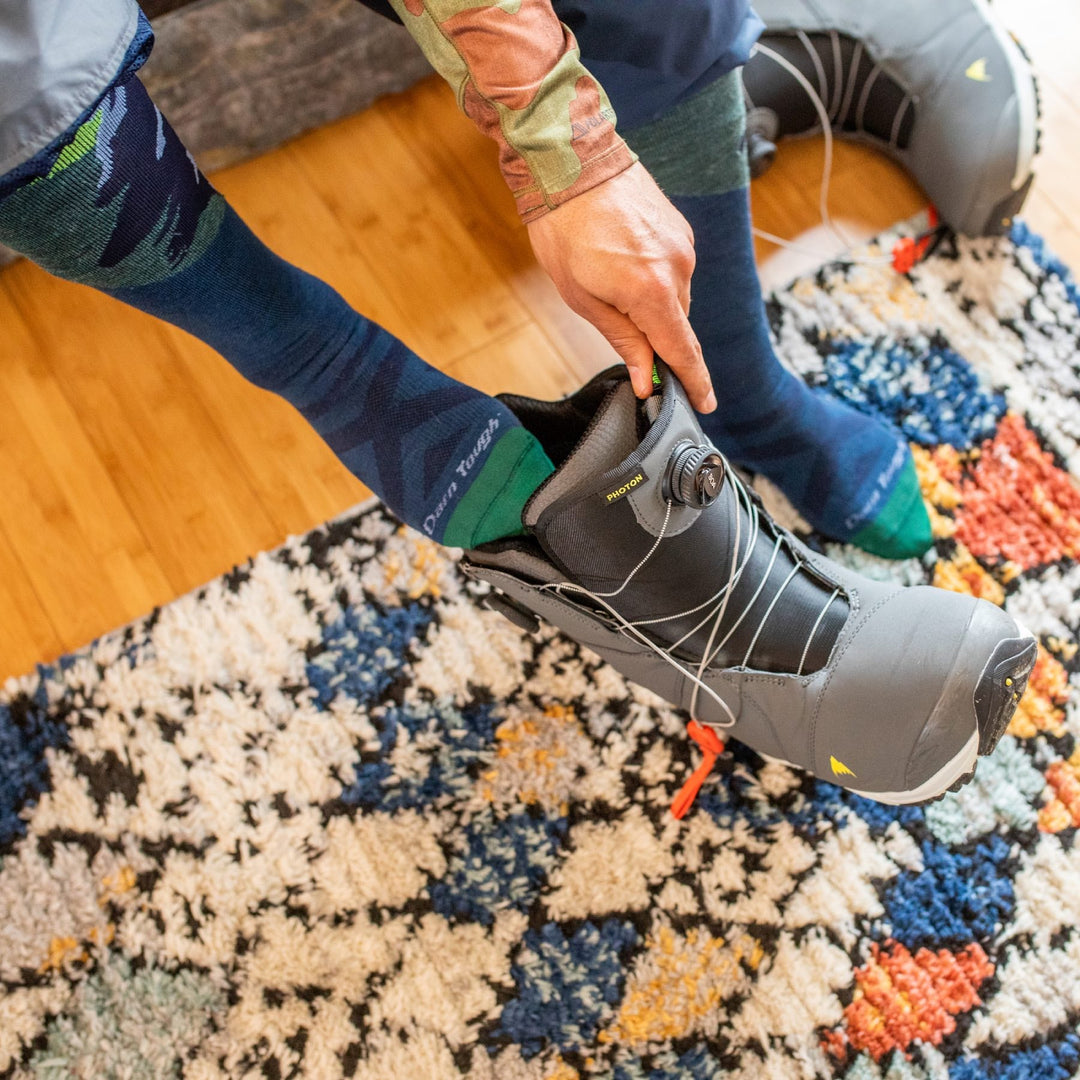 Snowboarder pulling off his snowboard boots, showing his darn tough anti-odor snowboard socks