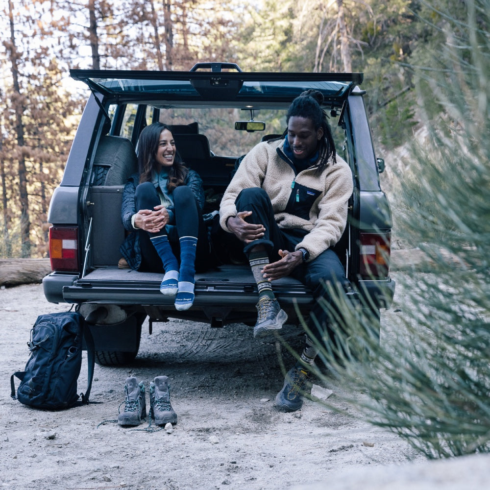 Two hikers seated in back of car pulling on hiking socks, talking about sock liners