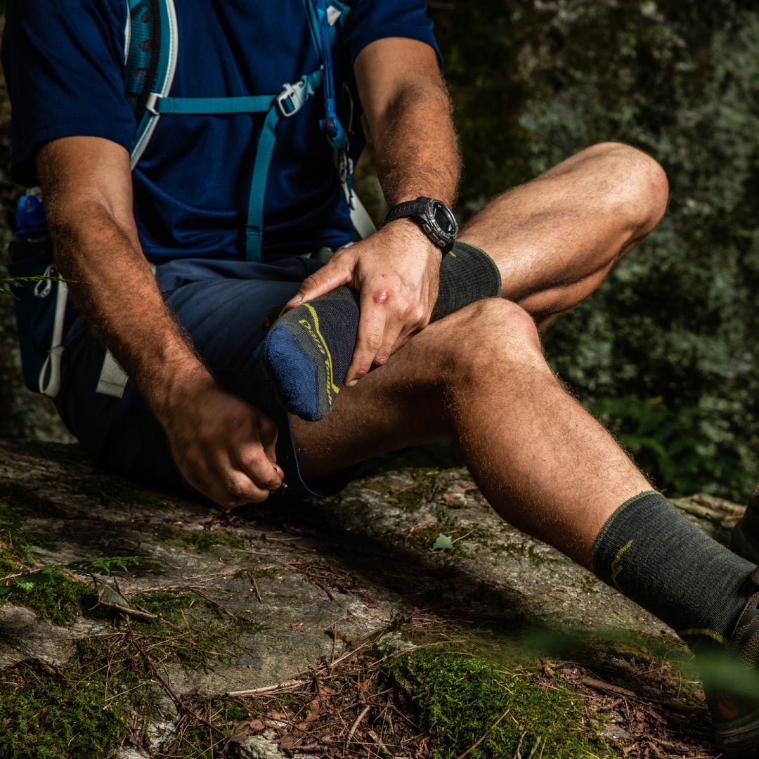 Hiker seated with boot off, checking his foot to prevent blisters