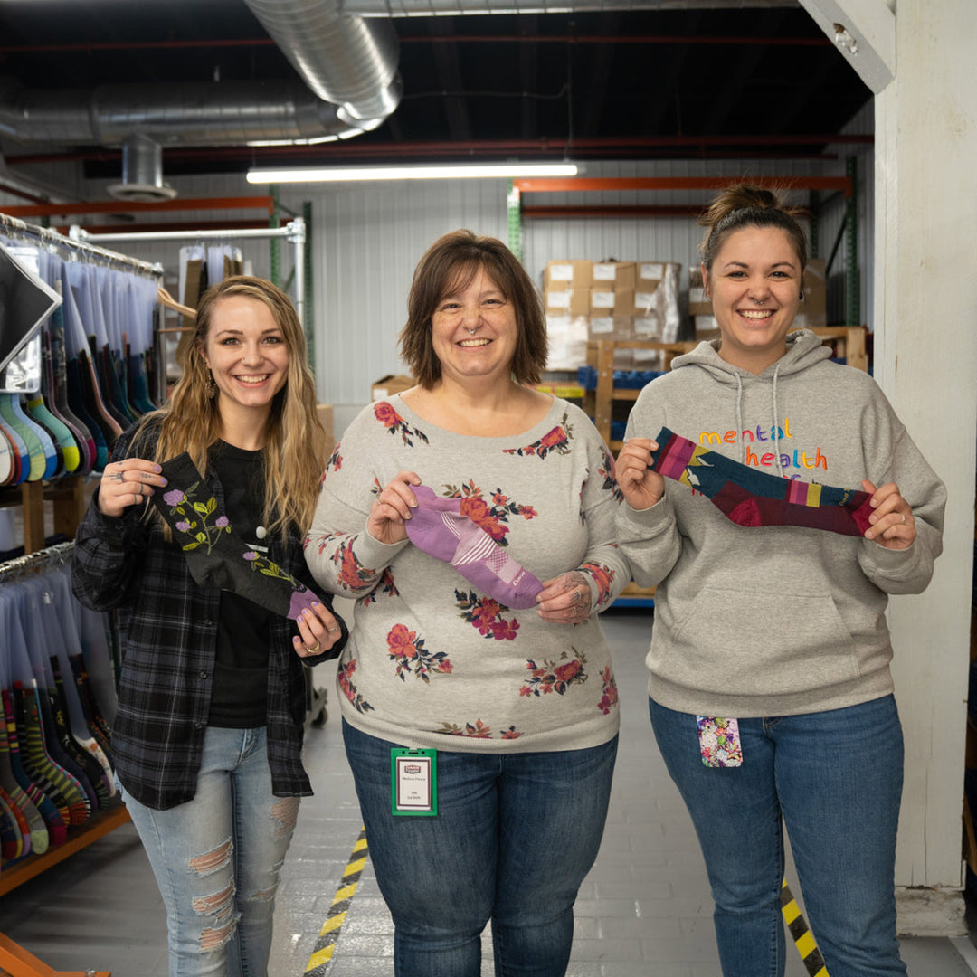 Two daughters standing with their mom, showing what socks they'd buy her for mother's day