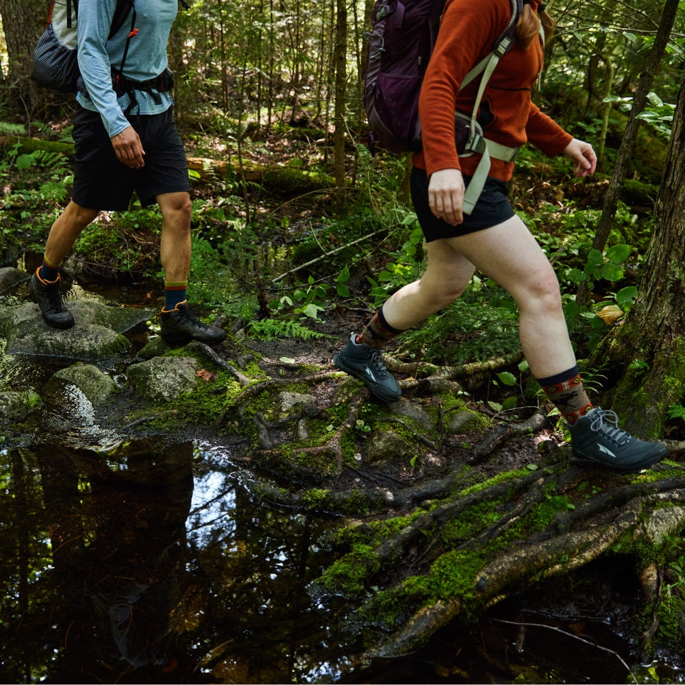 Two hikers walking down a swampy trail, the focus on their feet