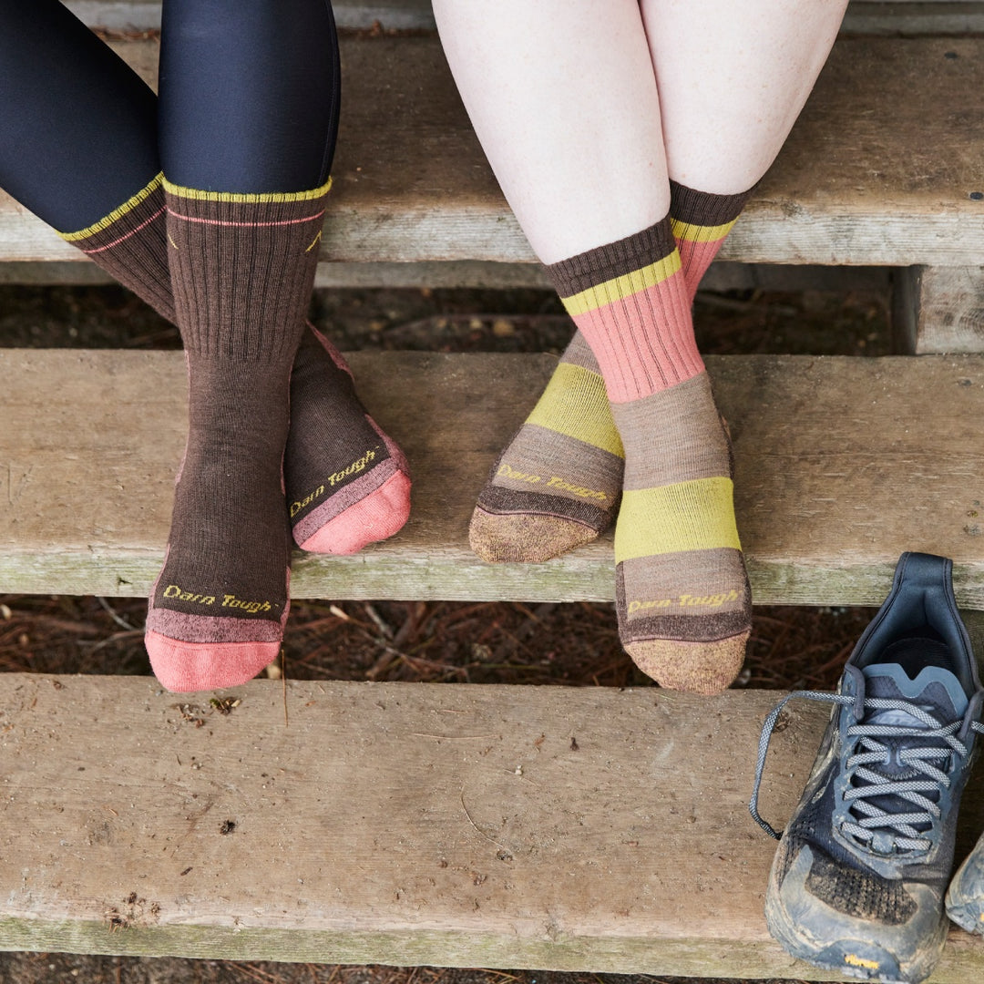 Two pairs of feet wearing merino wool hiking socks in brown and pink