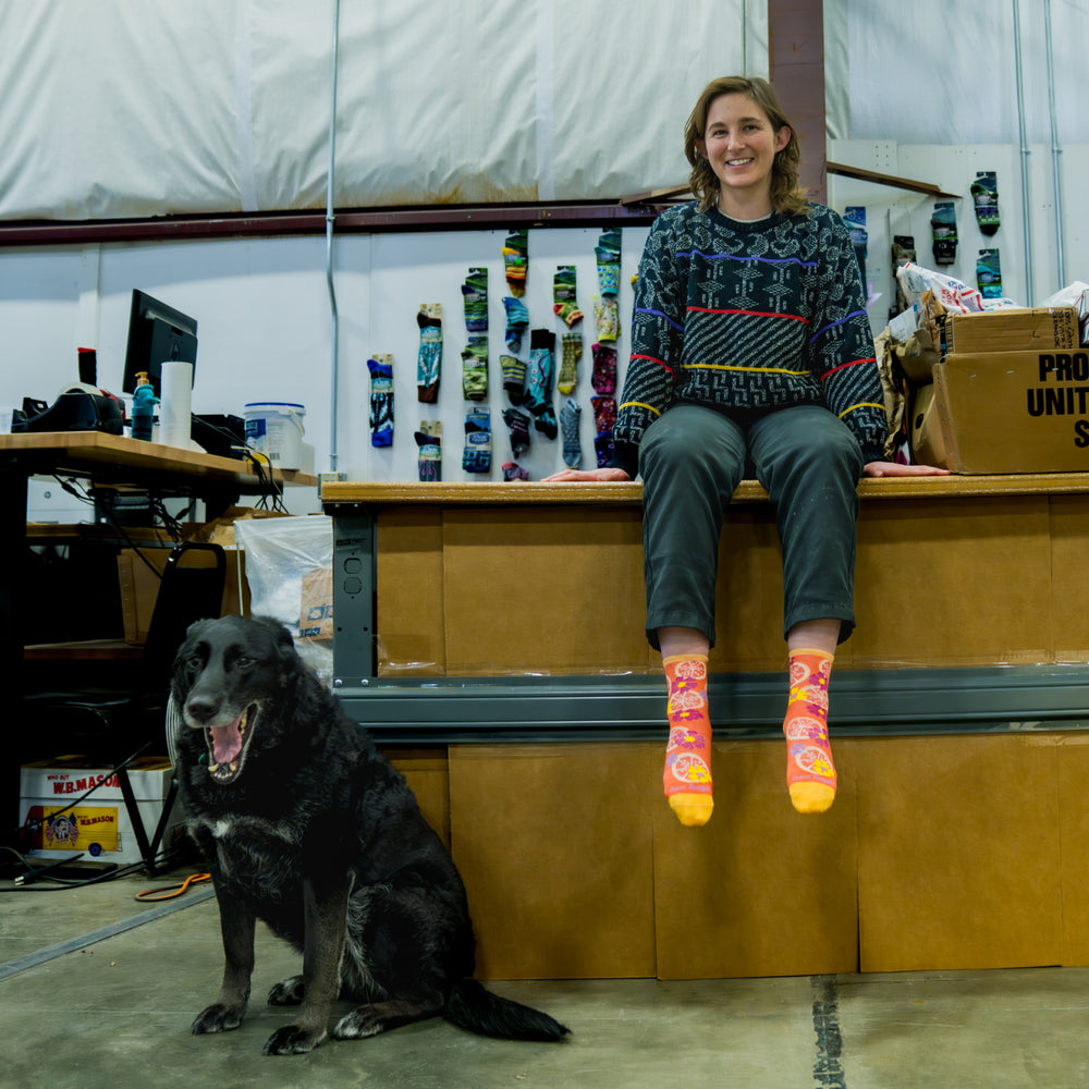 Emily sitting on her desk wearing her favorite socks with her dog nearby